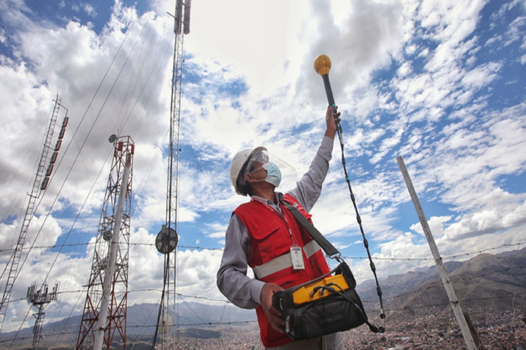 Técnico midiendo radiaciones no ionizantes con una sonda de campo junto a torres de telecomunicaciones en una zona alta